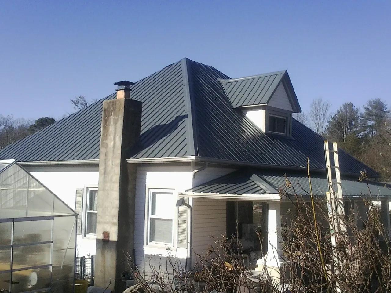 Dark blue standing seam metal roof on a white farmhouse with dormer — Slate & Tile Roof Repair by Roofing Brothers in Grove