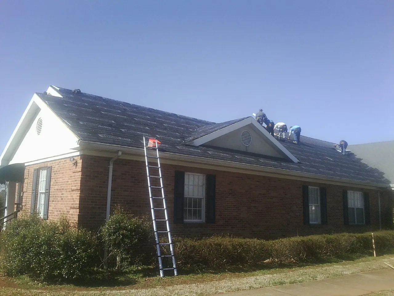 Crew tearing shingles off a brick ranch roof with a ladder set — Emergency Roof Repair work by our crew in Grove