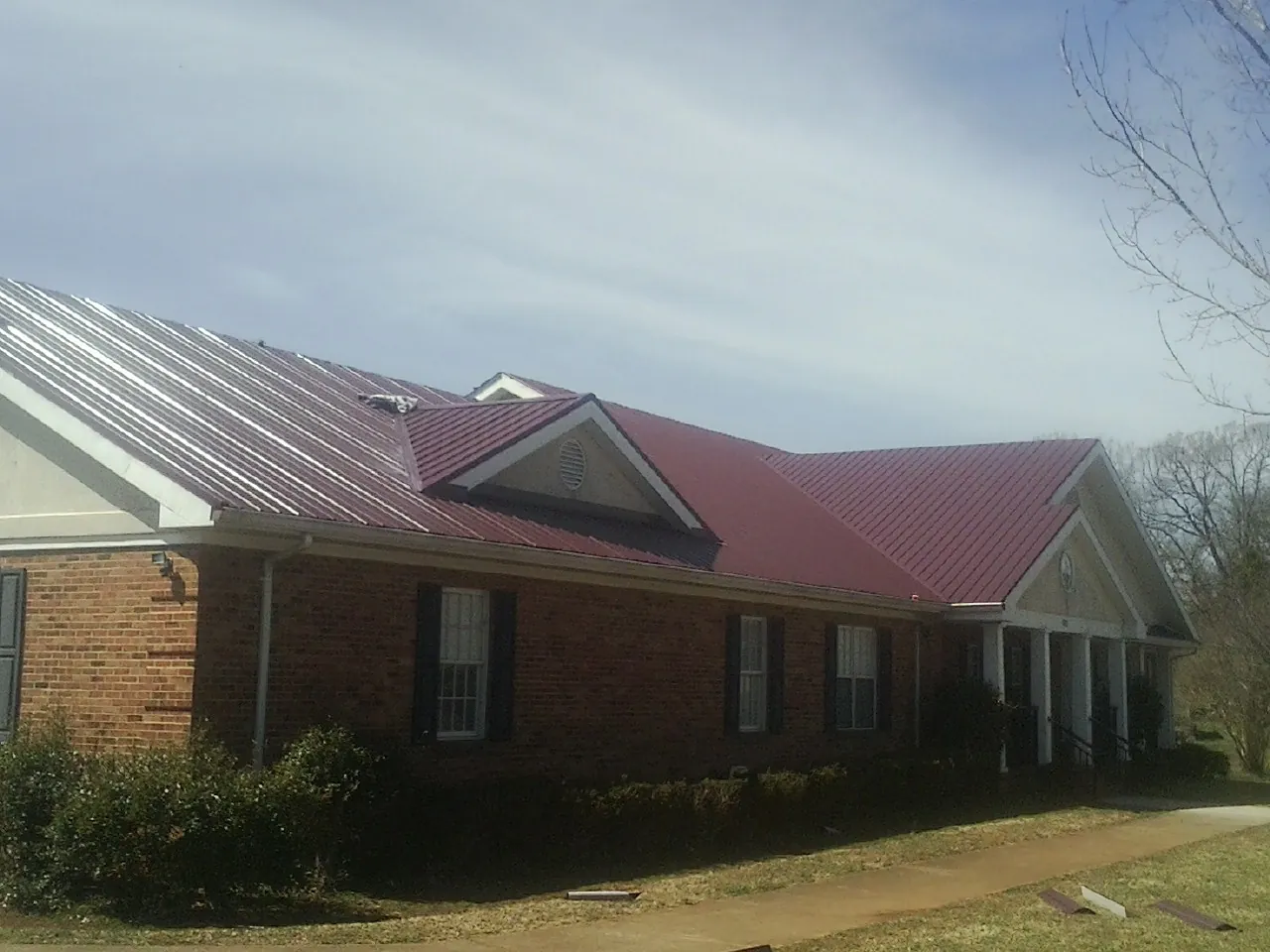 Red metal roof with gabled entries on a long brick building, from a Hail Damage Roof Repair job in Grove