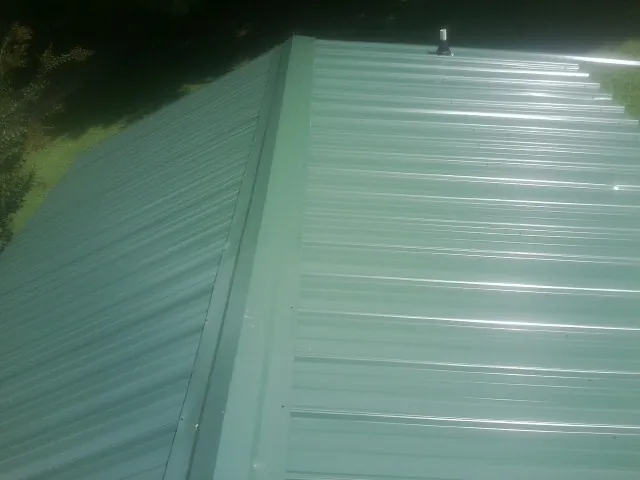 New green metal panels meeting at the ridge of a roof — Flat Roof Repair work by our crew in Grove