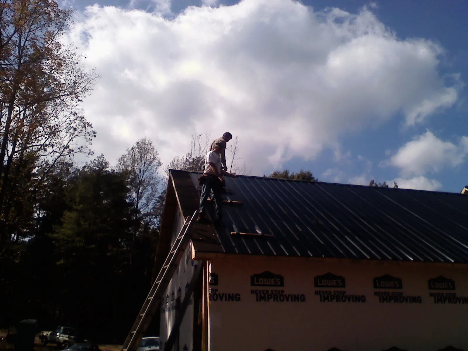 Roofer fastening dark metal panels high against a cloudy sky, from a Roof Inspection job in Grove