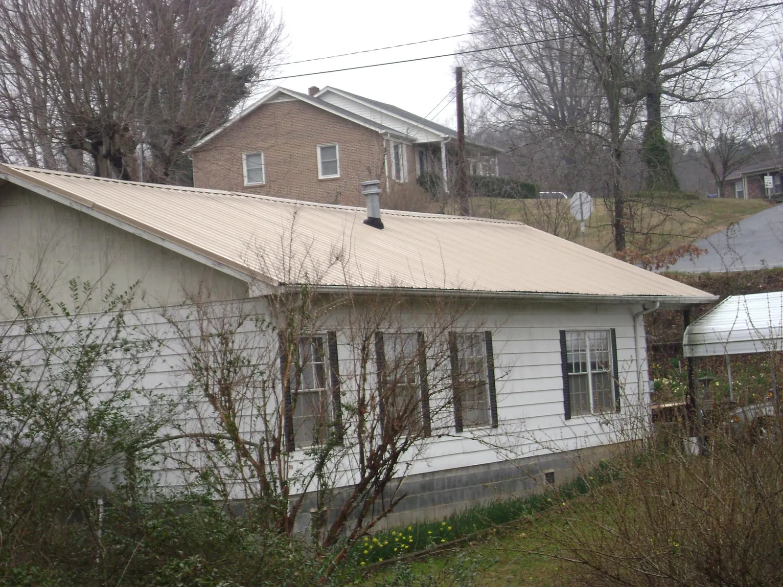 Tan metal roof on a white sided house set into a hillside — Commercial Roofing by Roofing Brothers in Grove