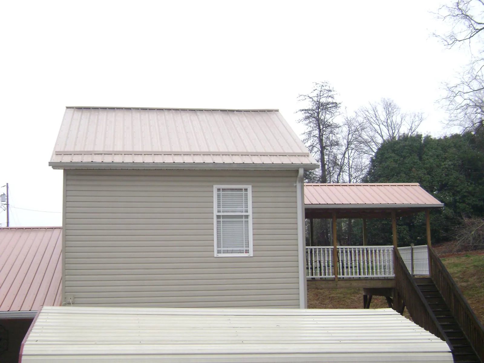 Tan metal roofs on a two story addition and attached porch, from a Roof Replacement job in Grove